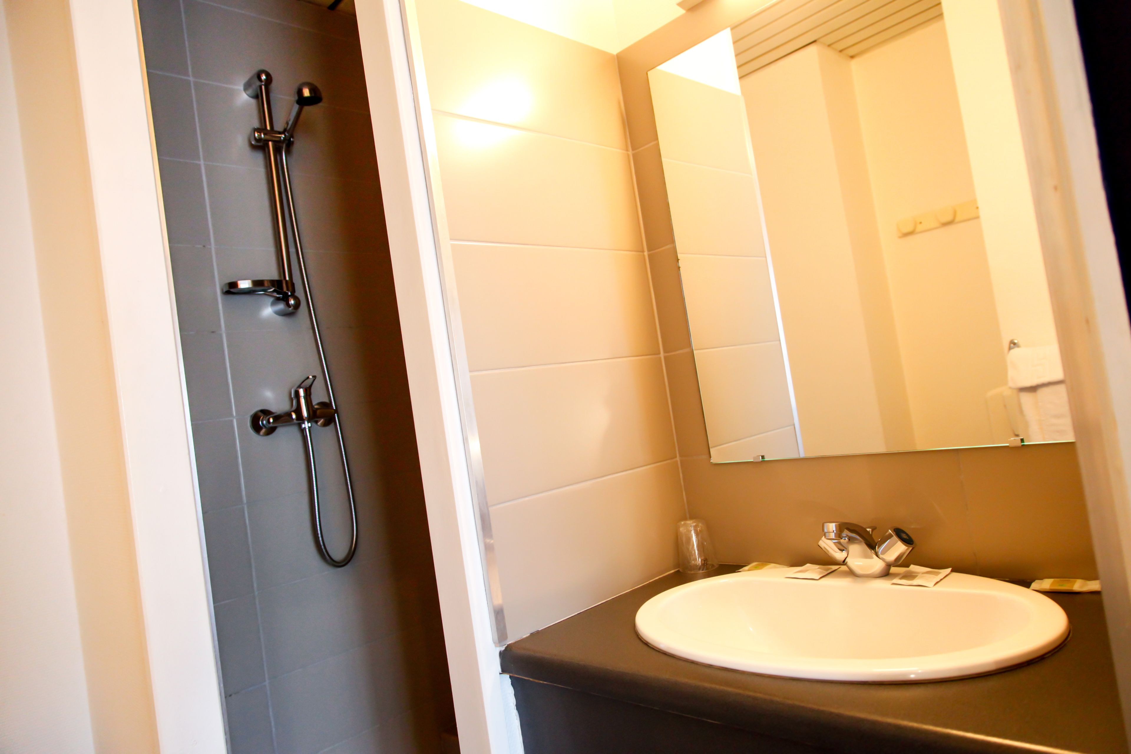 Een badkamer met douche, wastafel en spiegel.
