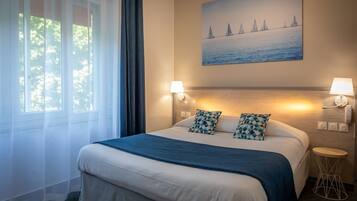 Habitación de hotel con una cama grande, dos lámparas de pared, un cuadro de veleros y una mesita redonda.
