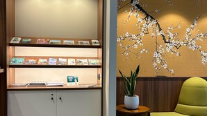 A reception area with a wooden cabinet displaying brochures, a potted plant, and a green armchair. - Rex Hotel (Lorient)
