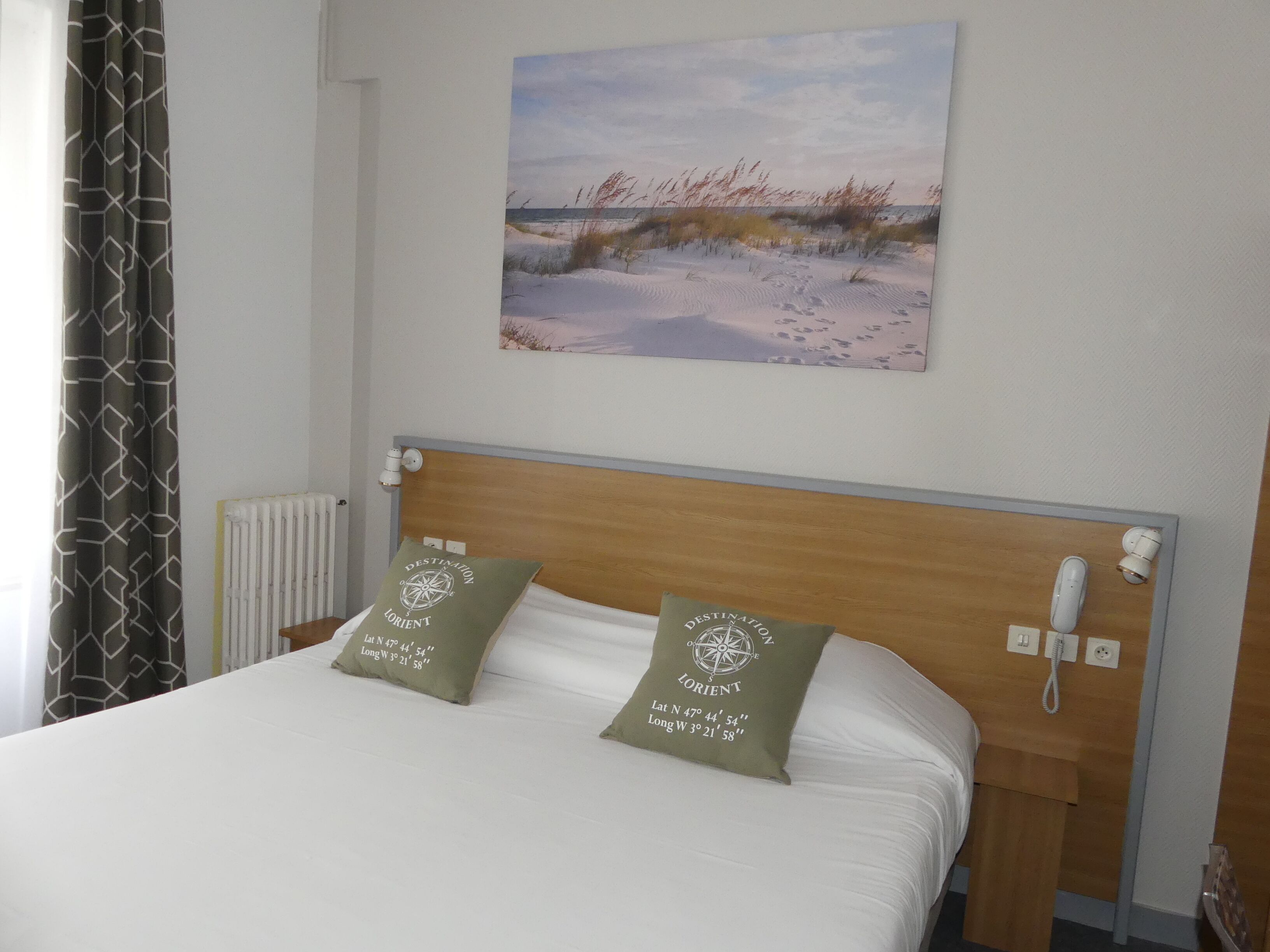Een hotelkamer met een bed, twee kussens, een schilderij aan de muur, een telefoon en een radiator.