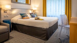 A hotel room with a large bed, two bedside lamps, a mirror above the bed, a chair, and a desk with a lamp. - Rex Hotel (Lorient)