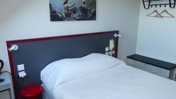 Una habitación de hotel con una cama, un taburete rojo, un teléfono y un cuadro en la pared.