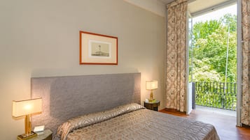 A hotel room with a large bed, two bedside lamps, a framed picture on the wall, and a balcony with a view of greenery.