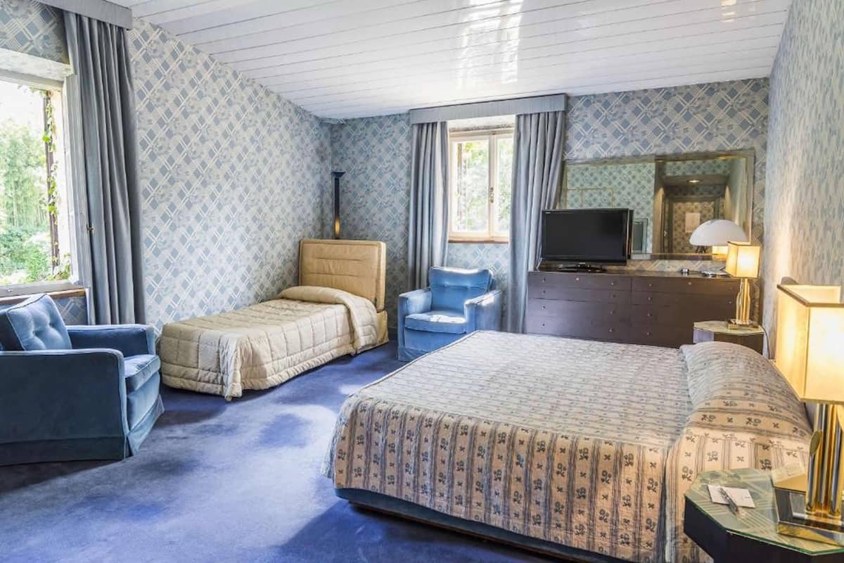 A hotel room with two beds, a TV, a desk with a lamp, and a large window.
