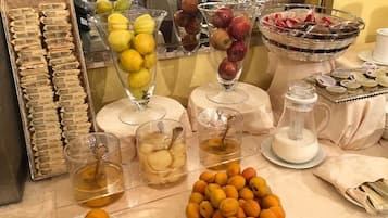 A buffet table with various food items including fruits, pastries, and beverages.