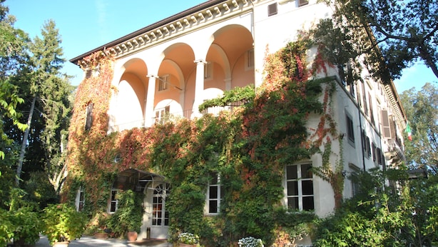 Un edificio con fachada blanca, varios arcos y muros cubiertos de hiedra.