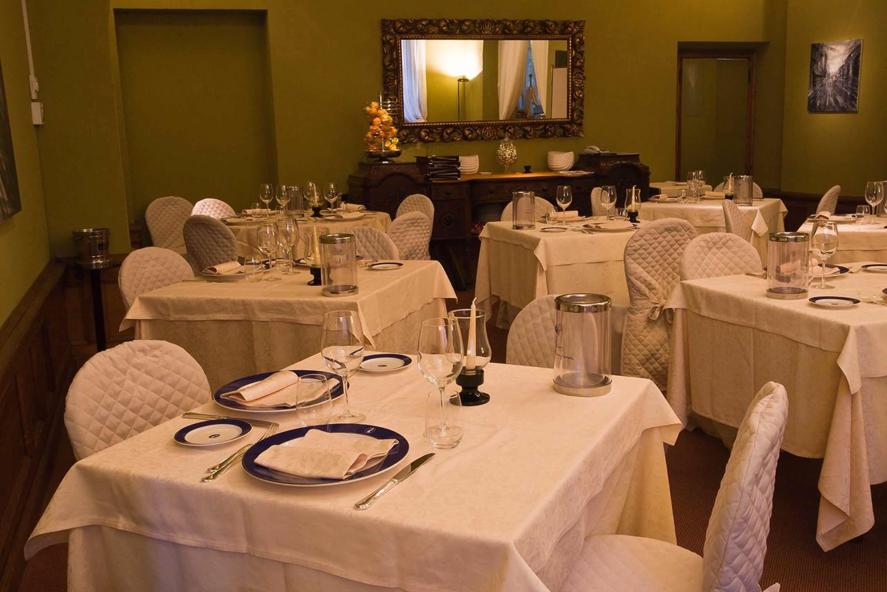 Un comedor con mesas dispuestas para el servicio, sillas y un espejo en la pared.