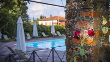 Un área junto a la piscina con un muro de ladrillo, rosales y sillones de descanso.