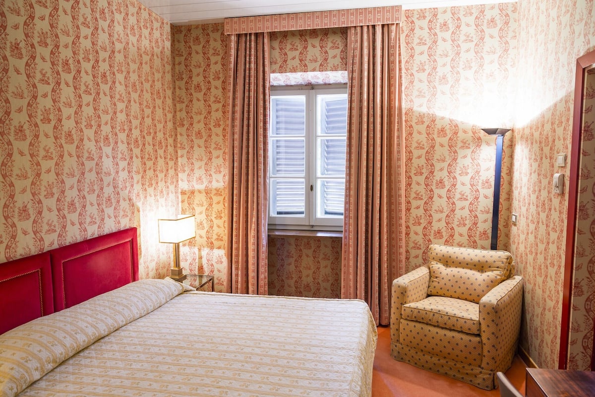 A hotel room with a bed, a chair, a lamp, and a window with curtains.