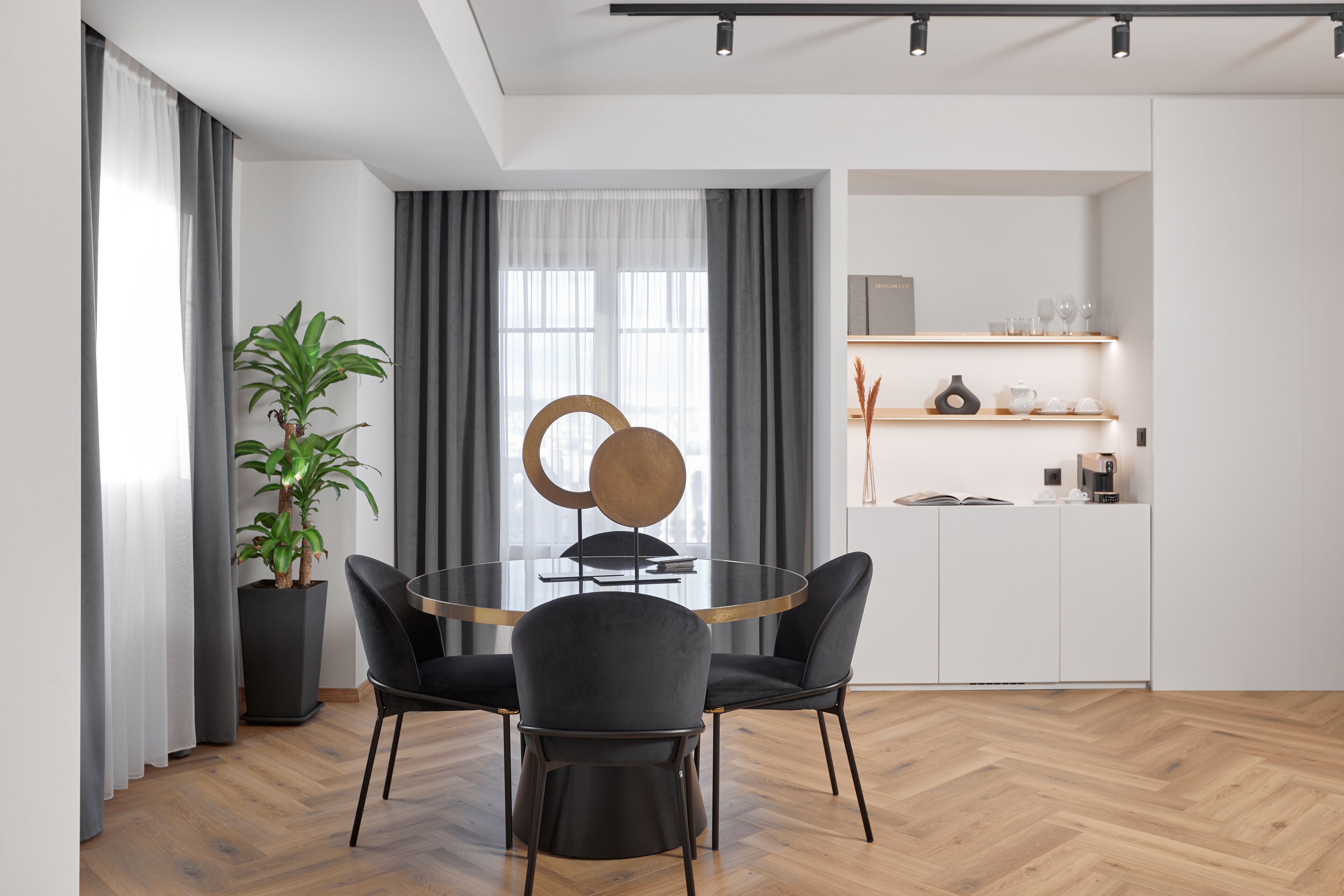 A modern dining area with a round table, black chairs, a potted plant, and a minimalist decor.