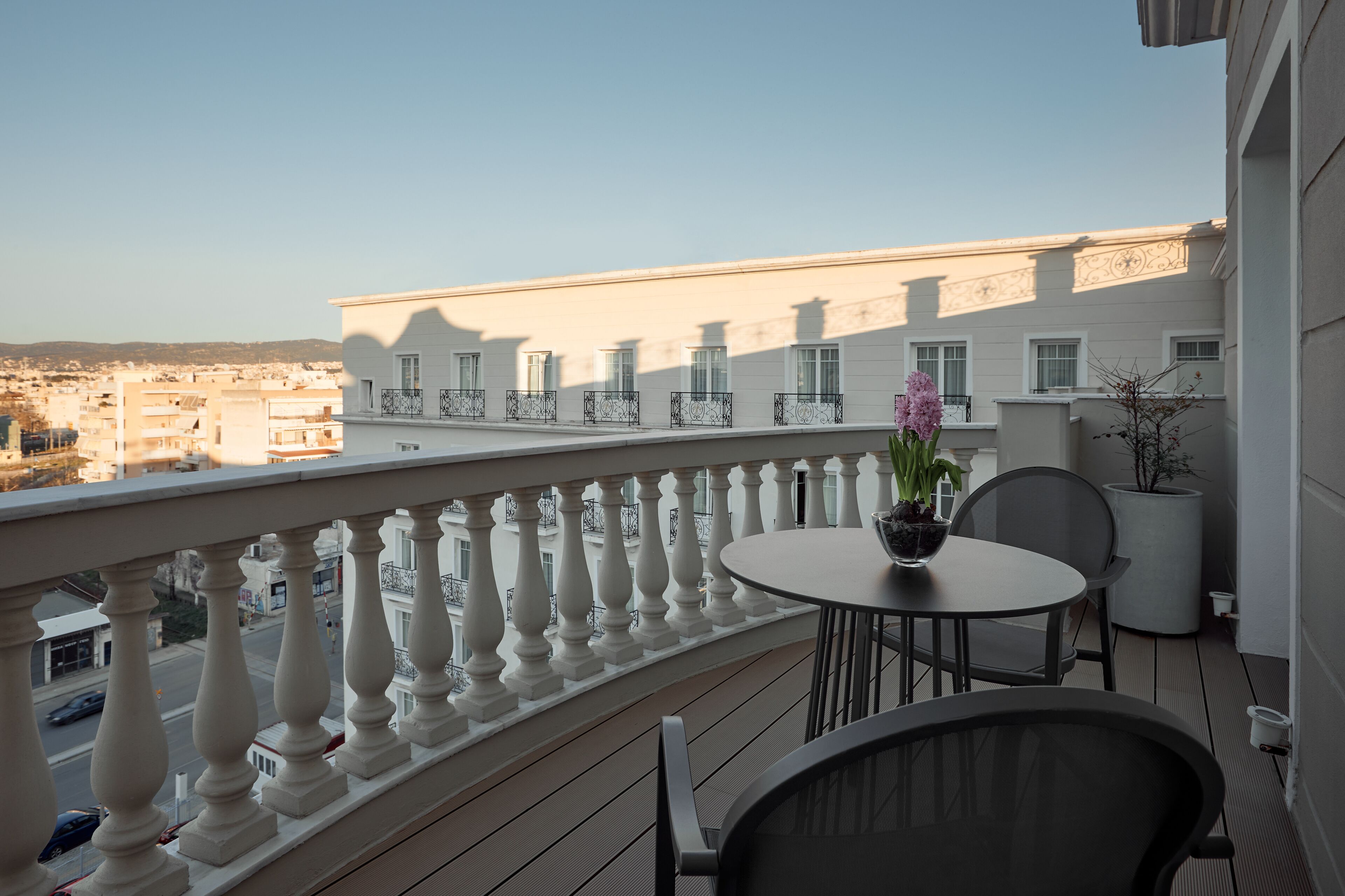 A balcony with a white balustrade, a round table with two chairs, and a potted plant.