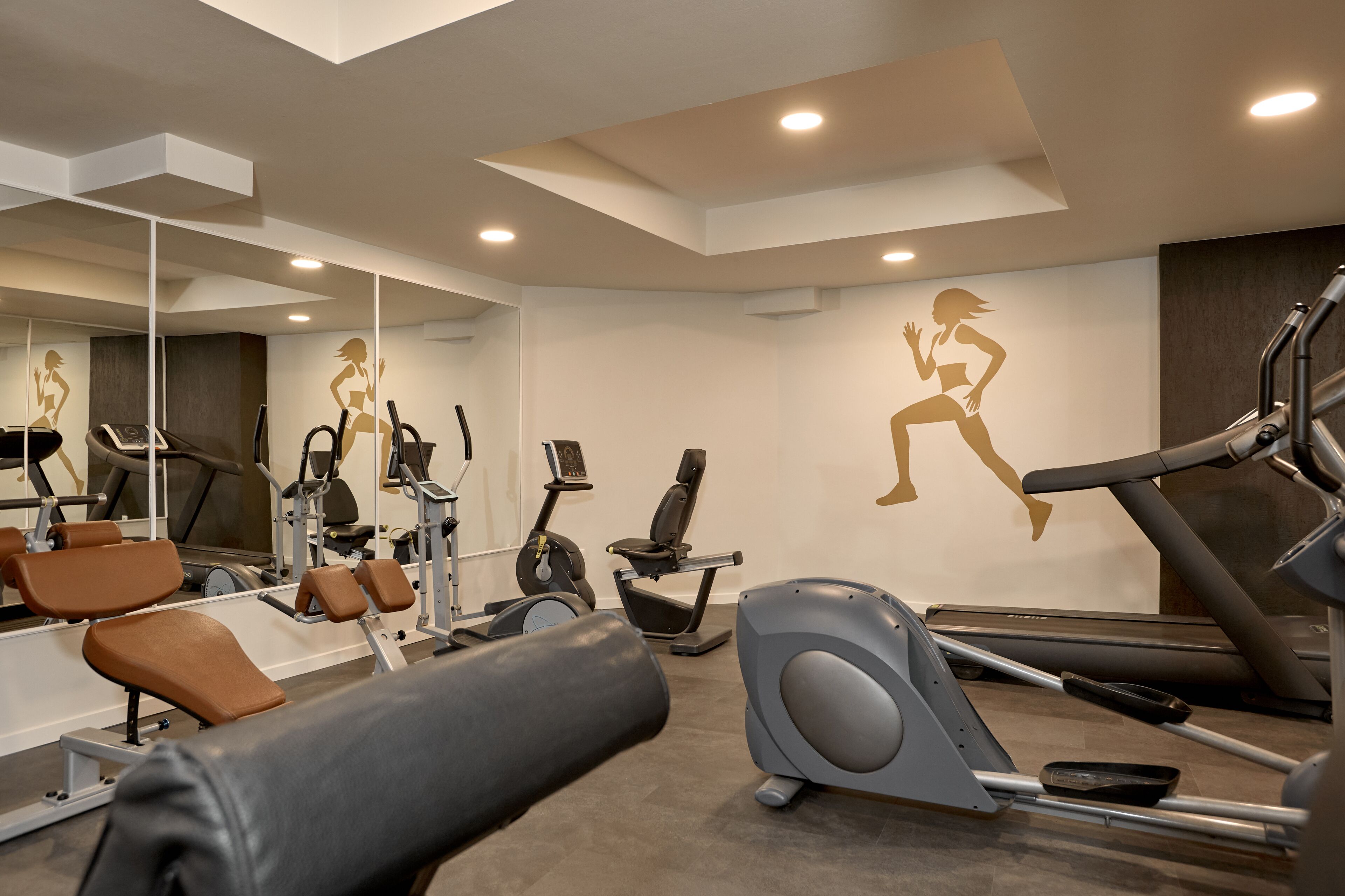 Un gimnasio moderno con diversos equipos de ejercicio, entre ellos cintas de correr y bicicletas estáticas, y espejos en las paredes.