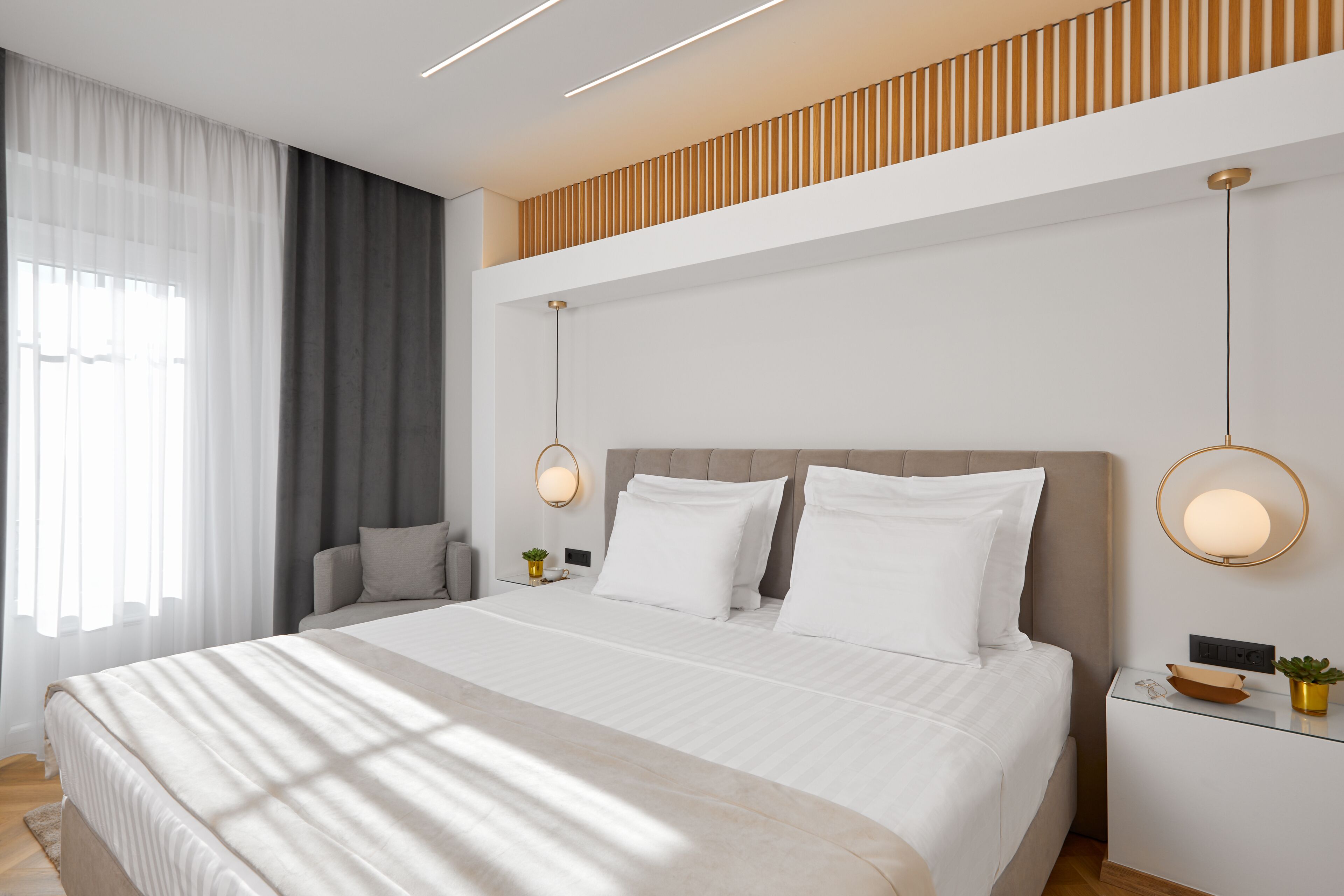 A modern bedroom with a large bed, bedside tables, a nightstand, and a window with curtains.
