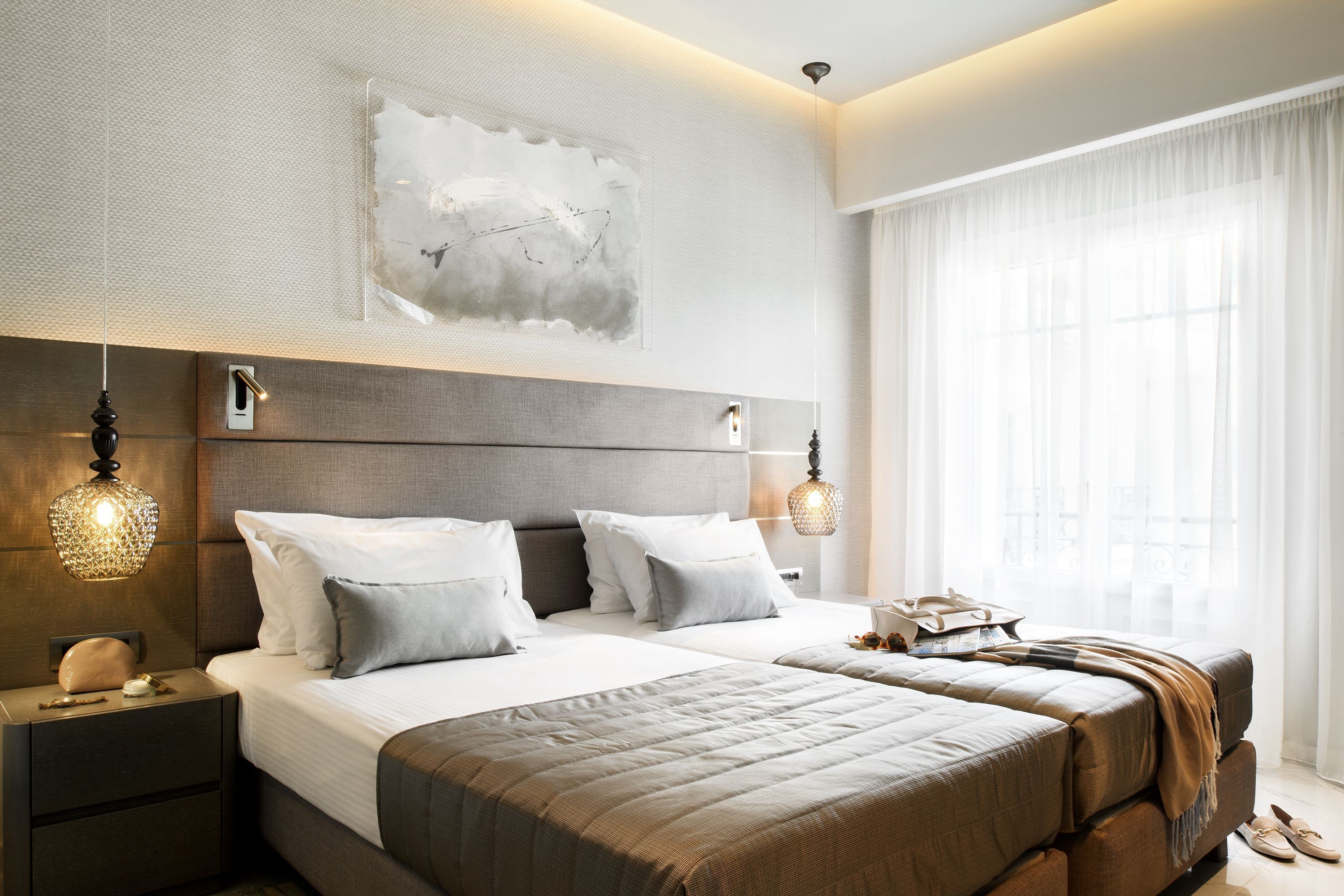 A modern bedroom with a large bed, bedside lamps, and a large window with sheer curtains.