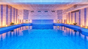 Una piscina interior con pared de mosaico azul, suelo de baldosas y luces empotradas.
