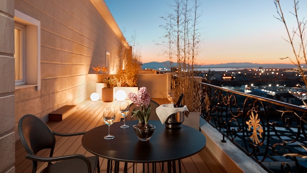 Una terraza con una mesa lista para dos personas, una botella de champán y un jarrón con flores.