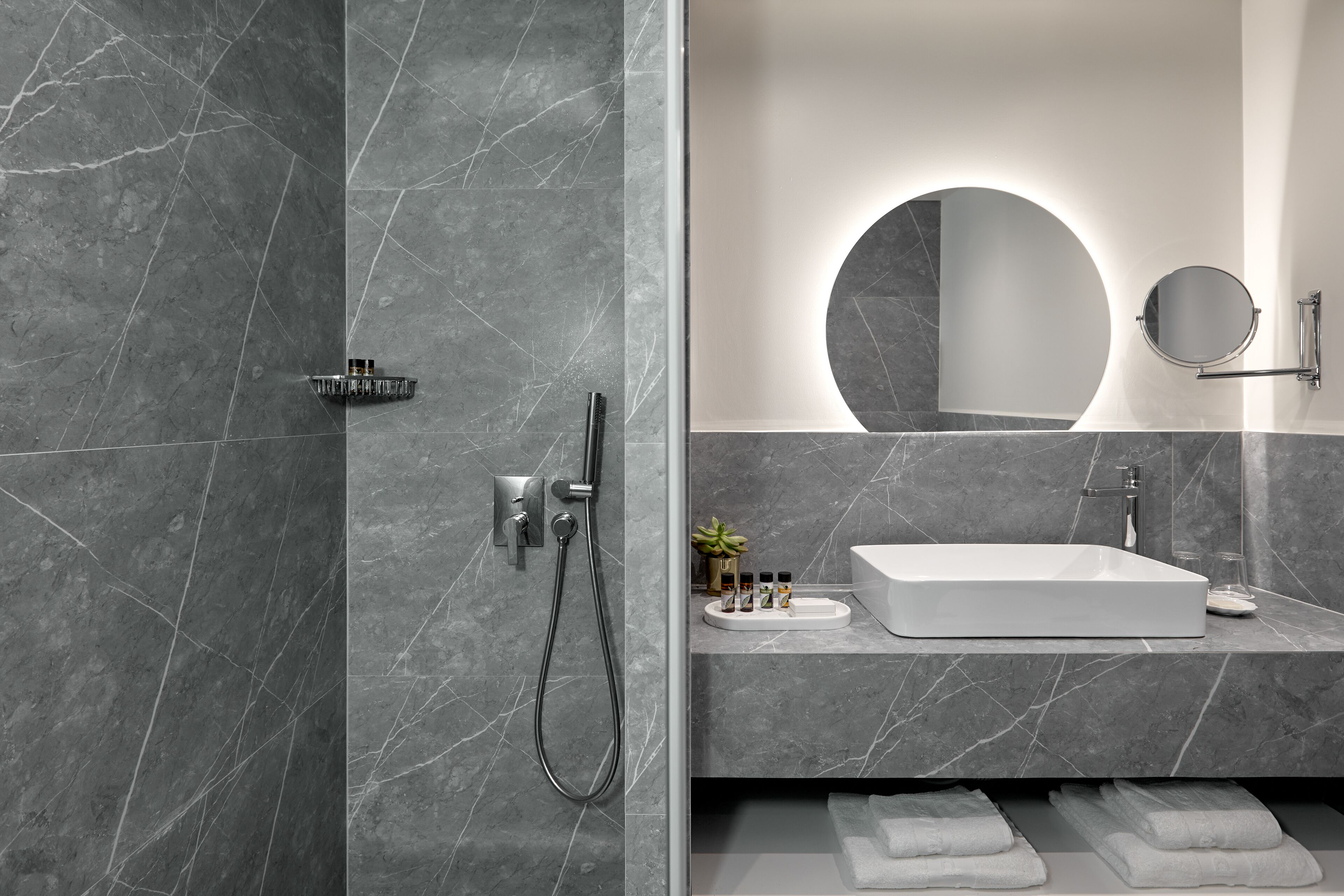 Un baño moderno con un lavamanos grande y rectangular, un espejo redondo y un cabezal de ducha de mano.