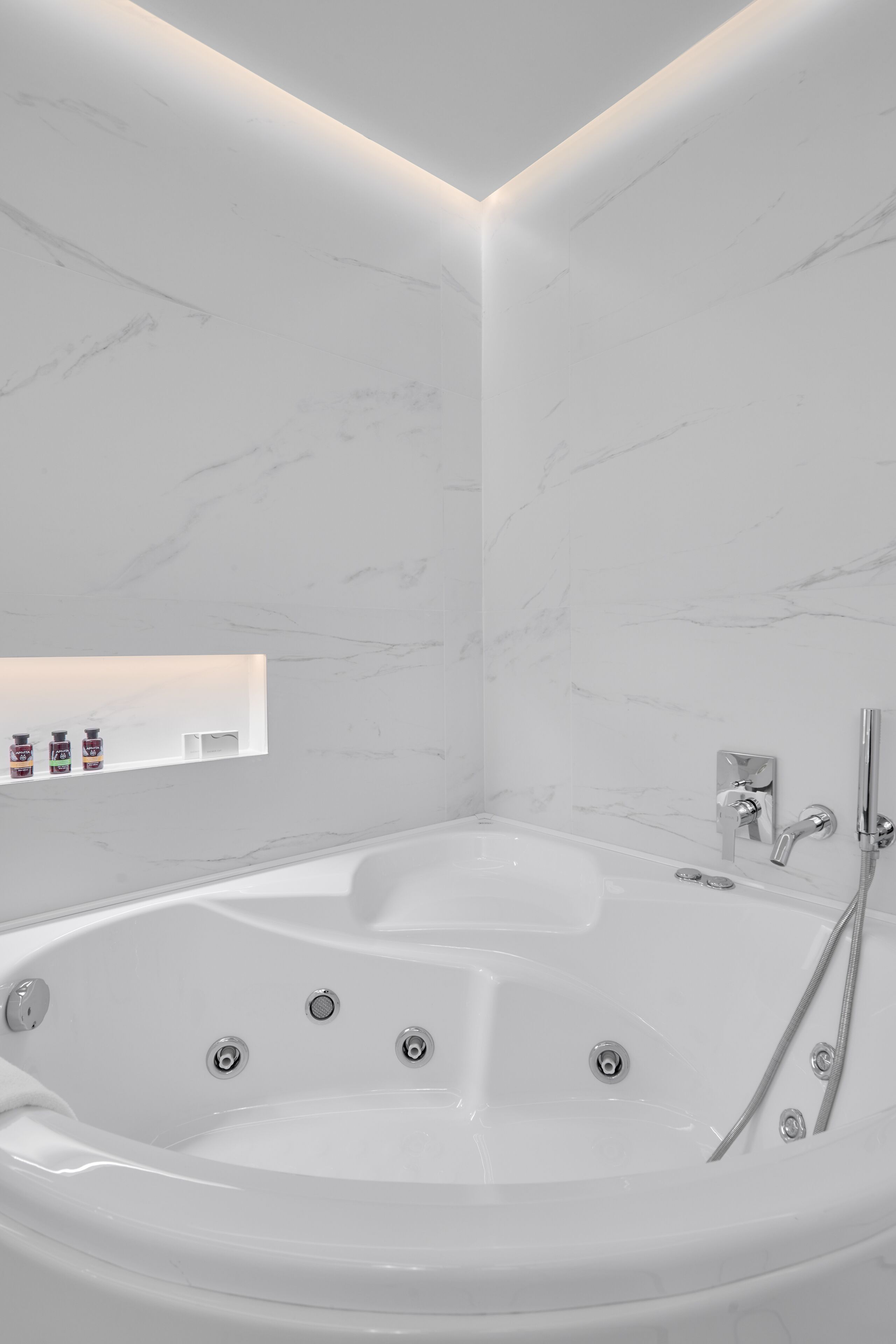 A modern bathroom with a large bathtub, a shower area, and a shelf with toiletries.