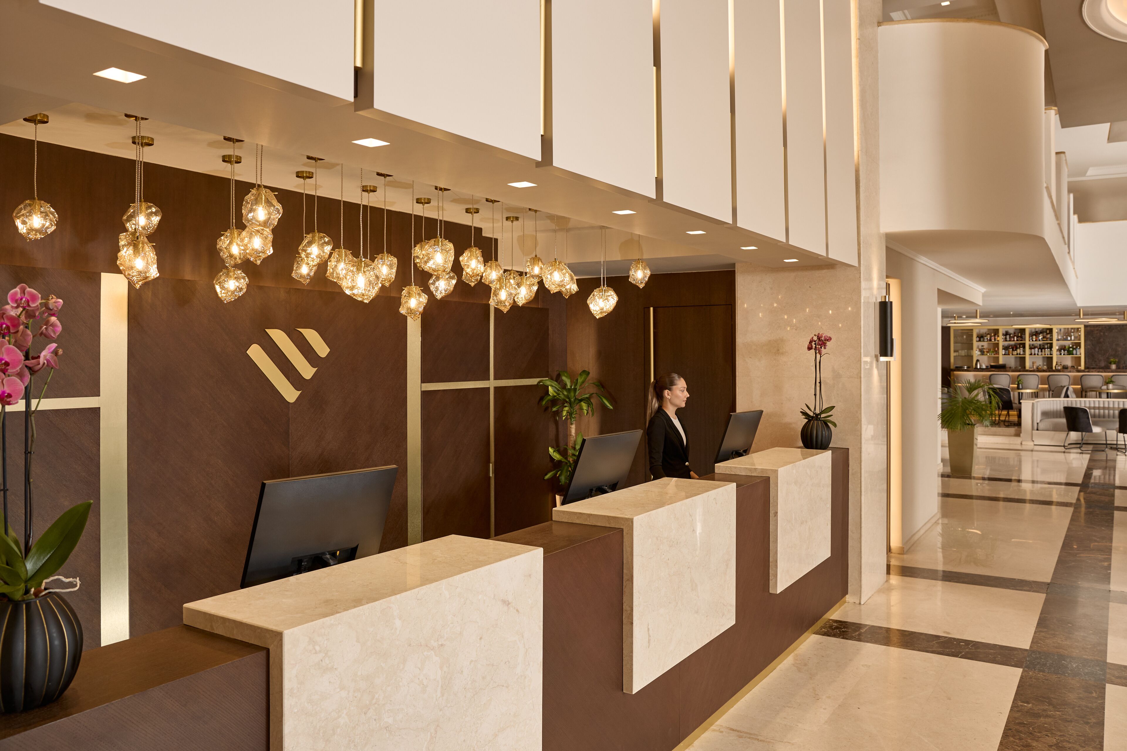 A modern reception area with marble counters, a receptionist, and decorative hanging lights.