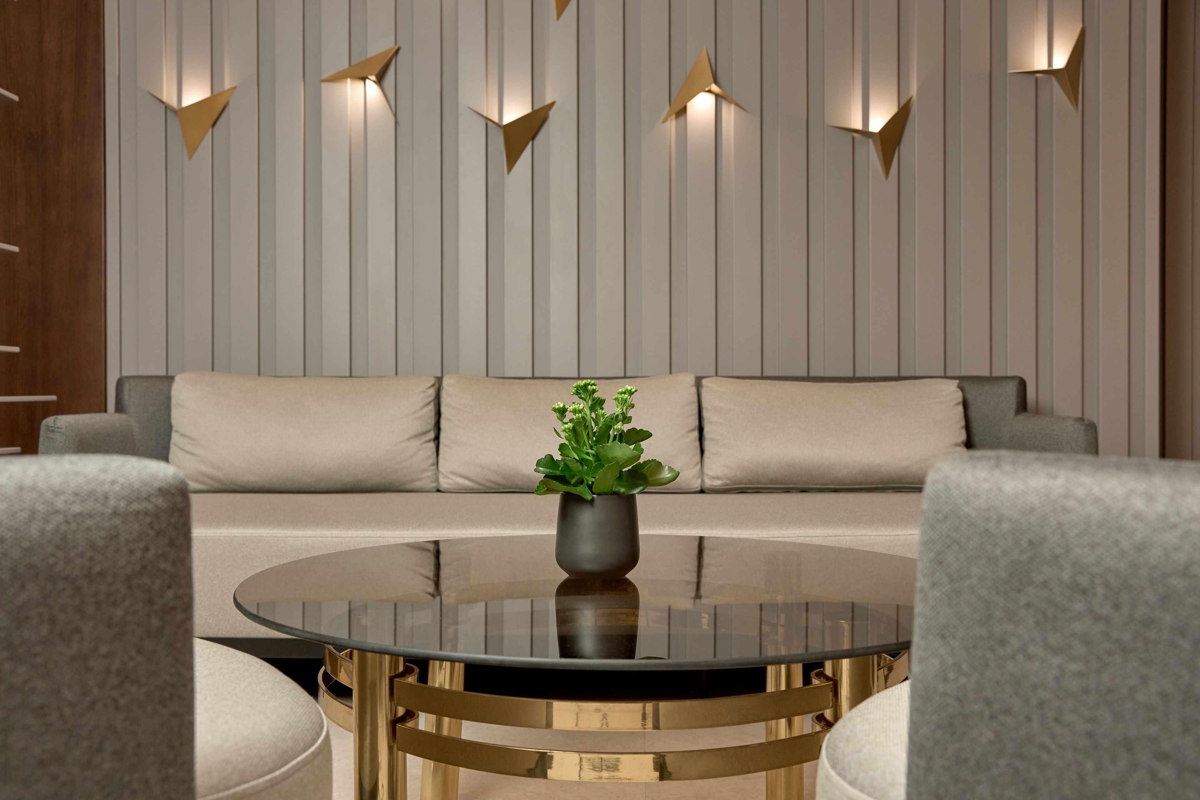 Un salon moderne avec un canapé, une table basse ronde en verre et des luminaires décoratifs fixés au mur.