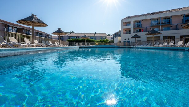 A clear blue pool with lounge chairs and umbrellas, surrounded by buildings with balconies. - Odalys Residence du port (Hourtin)