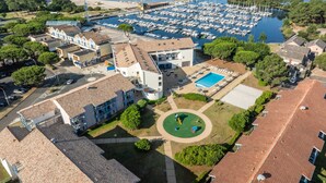 An aerial view of a coastal area with a marina, buildings, and a swimming pool. - Odalys Residence du port (Hourtin)