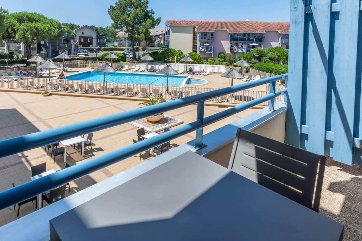 A pool area with lounge chairs and umbrellas, a table, and a railing.