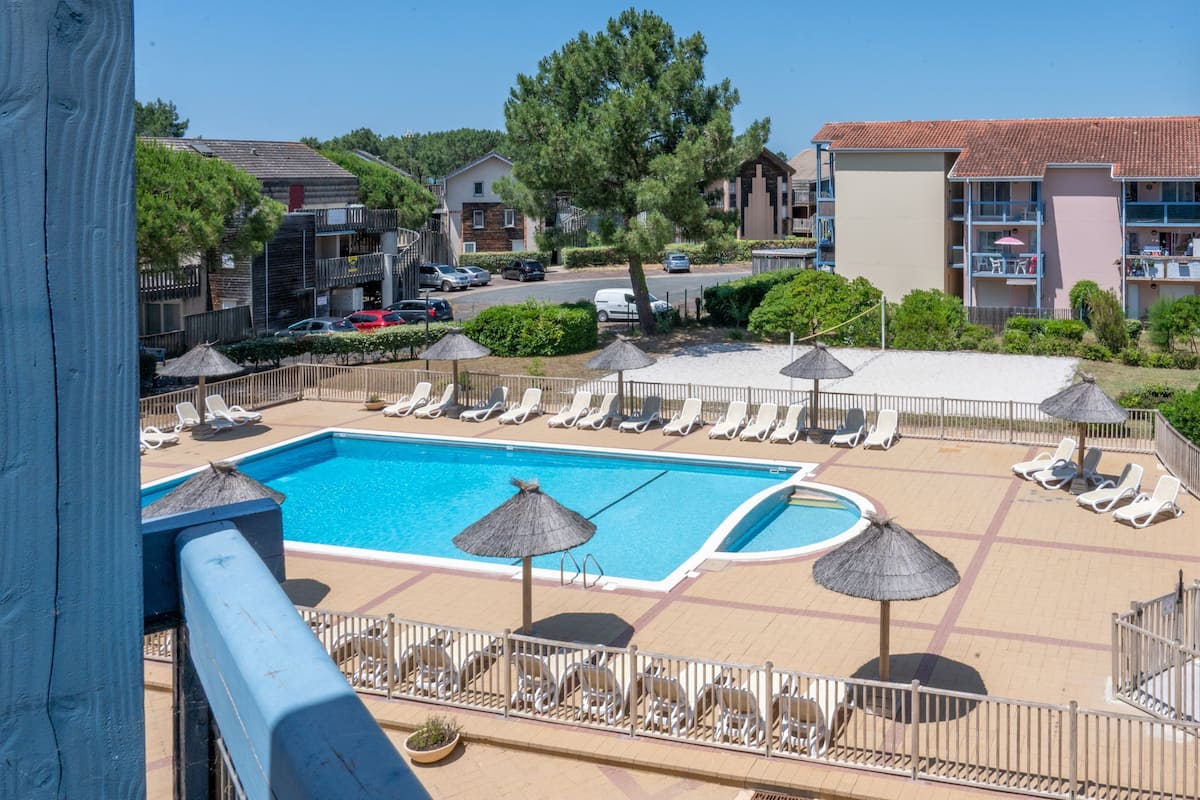 A pool area with lounge chairs and umbrellas, surrounded by buildings and a clear sky.