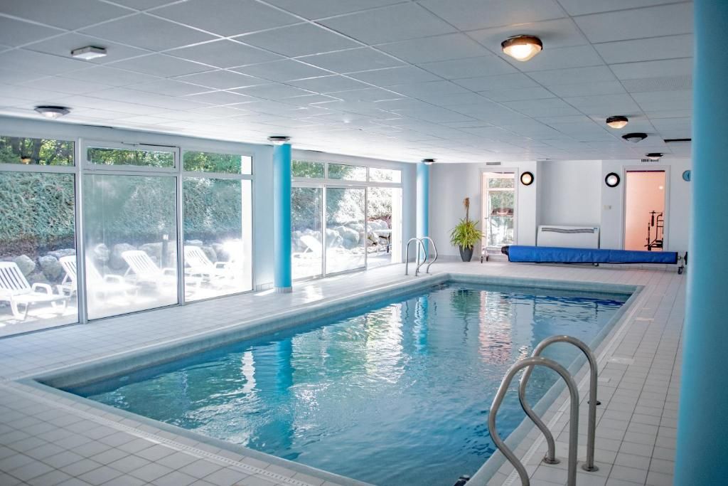 Una piscina interior con paredes de vidrio transparente, suelo de baldosas y zona junto a la piscina en azul.