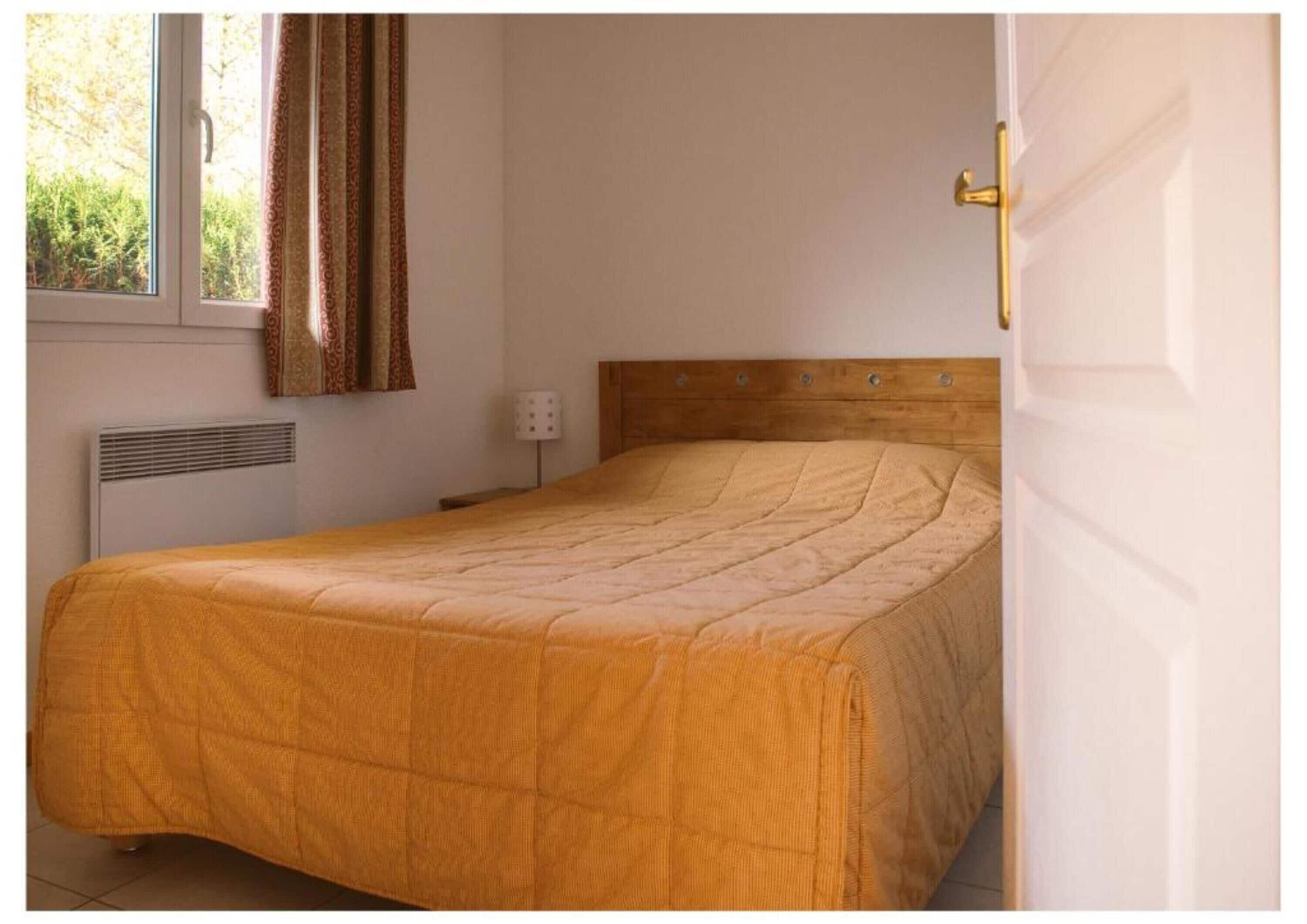 Una cama individual con cabecera de madera en una habitación con ventana y radiador.