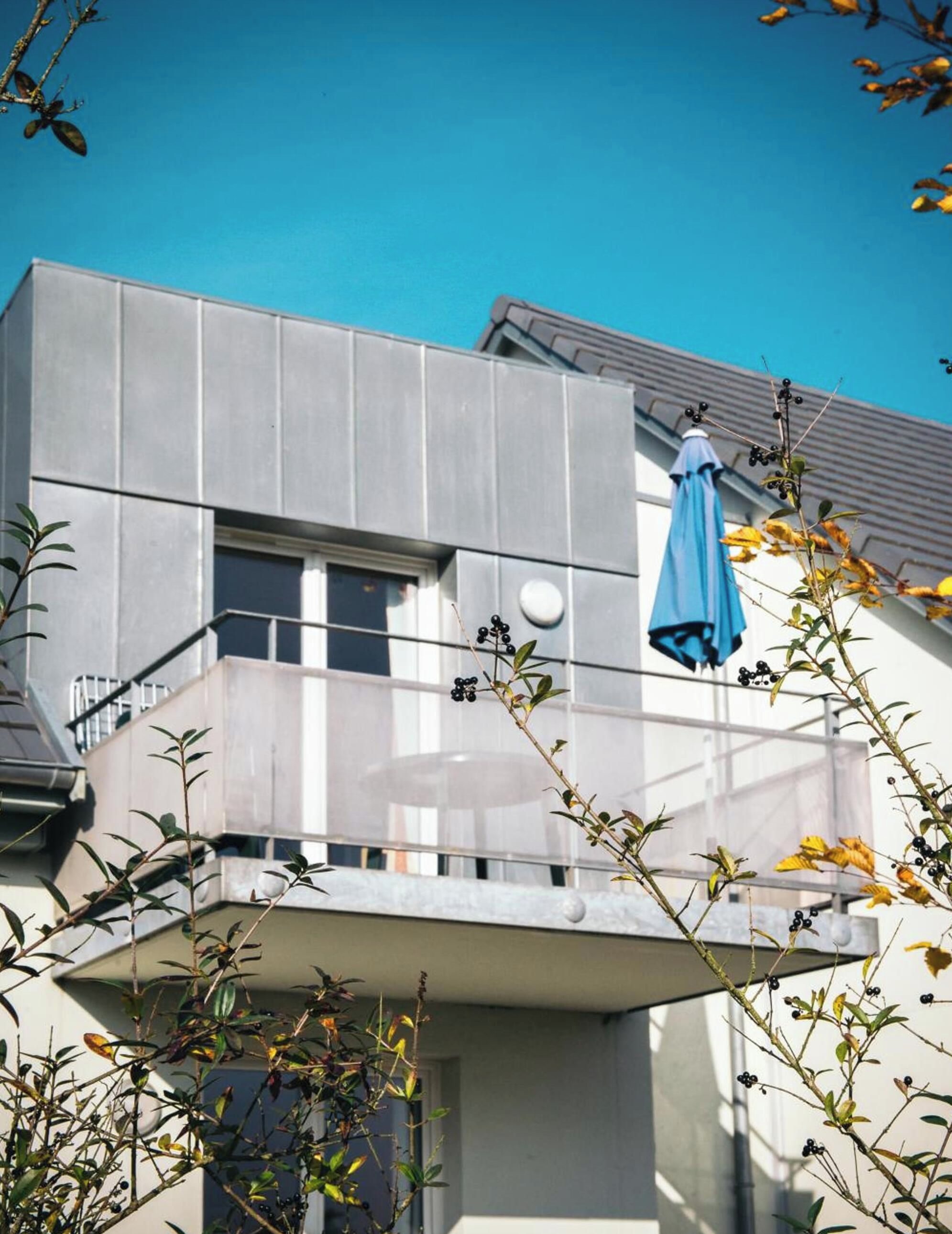 A modern building with a balcony, a blue umbrella, and some plants.