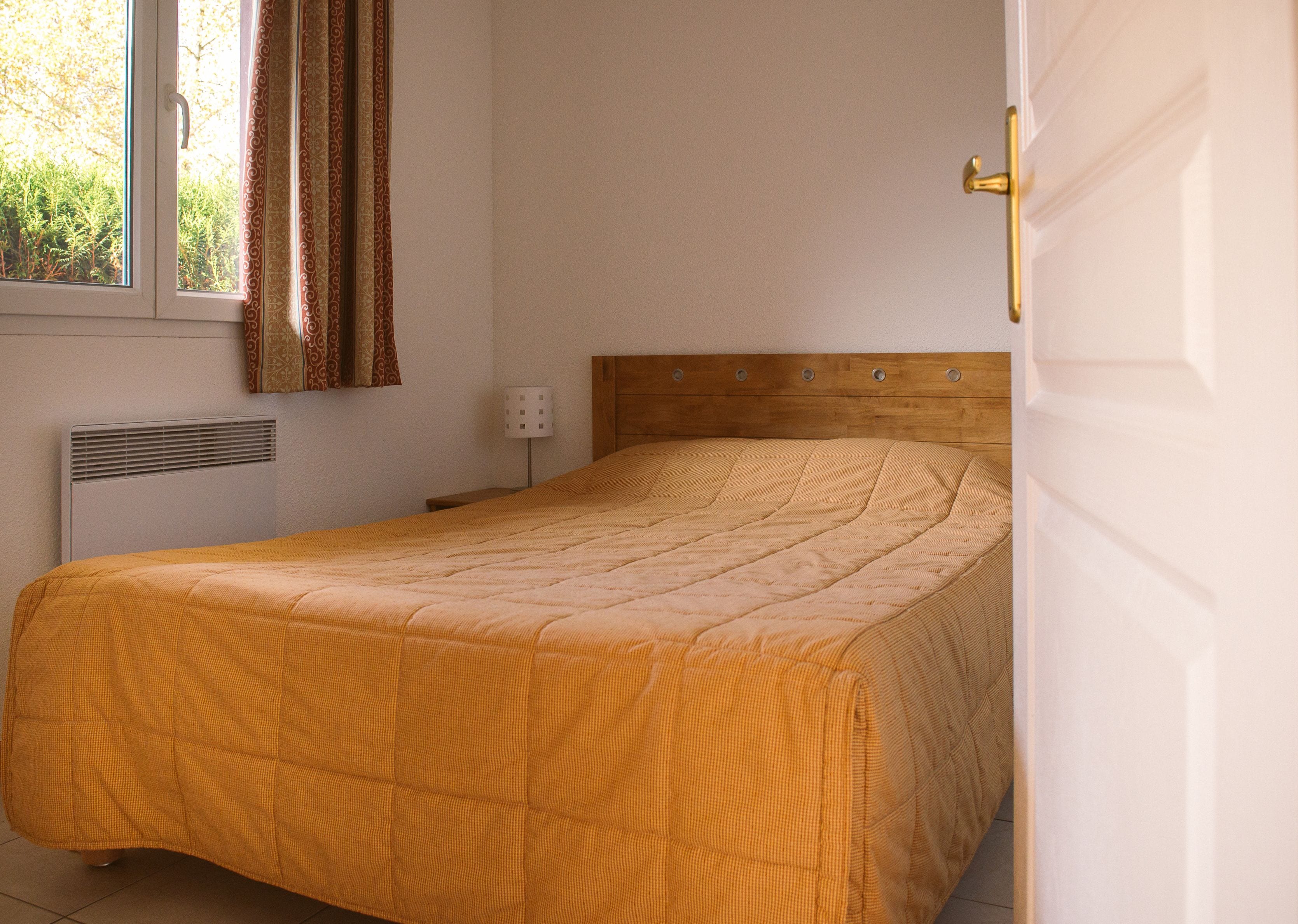 Ein Schlafzimmer mit einem Holz-Kopfteil, einem Bett mit einem gemusterten Überwurf, einem Heizkörper und einem Fenster mit Vorhängen.