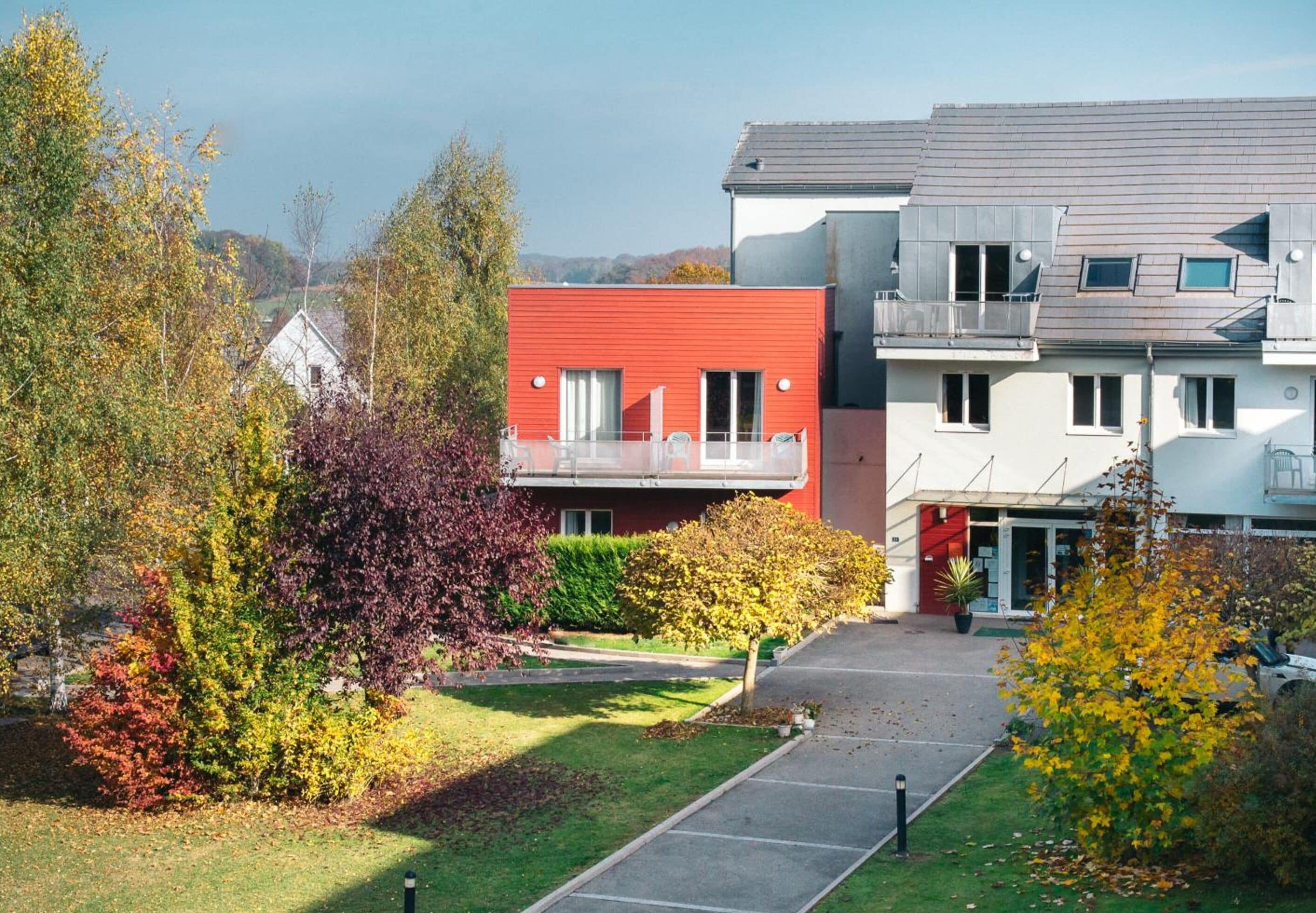 Ein modernes Wohngebäude mit roter Fassade, einem Balkon und einem Parkplatz.