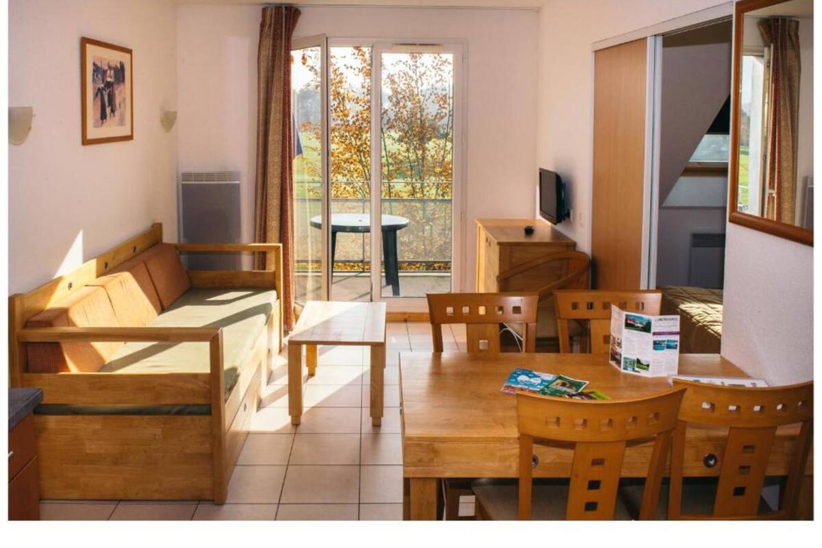 Um quarto acolhedor com um sofá de madeira, uma mesa de jantar com cadeiras, uma televisão pequena e uma porta de vidro deslizante para uma área externa.