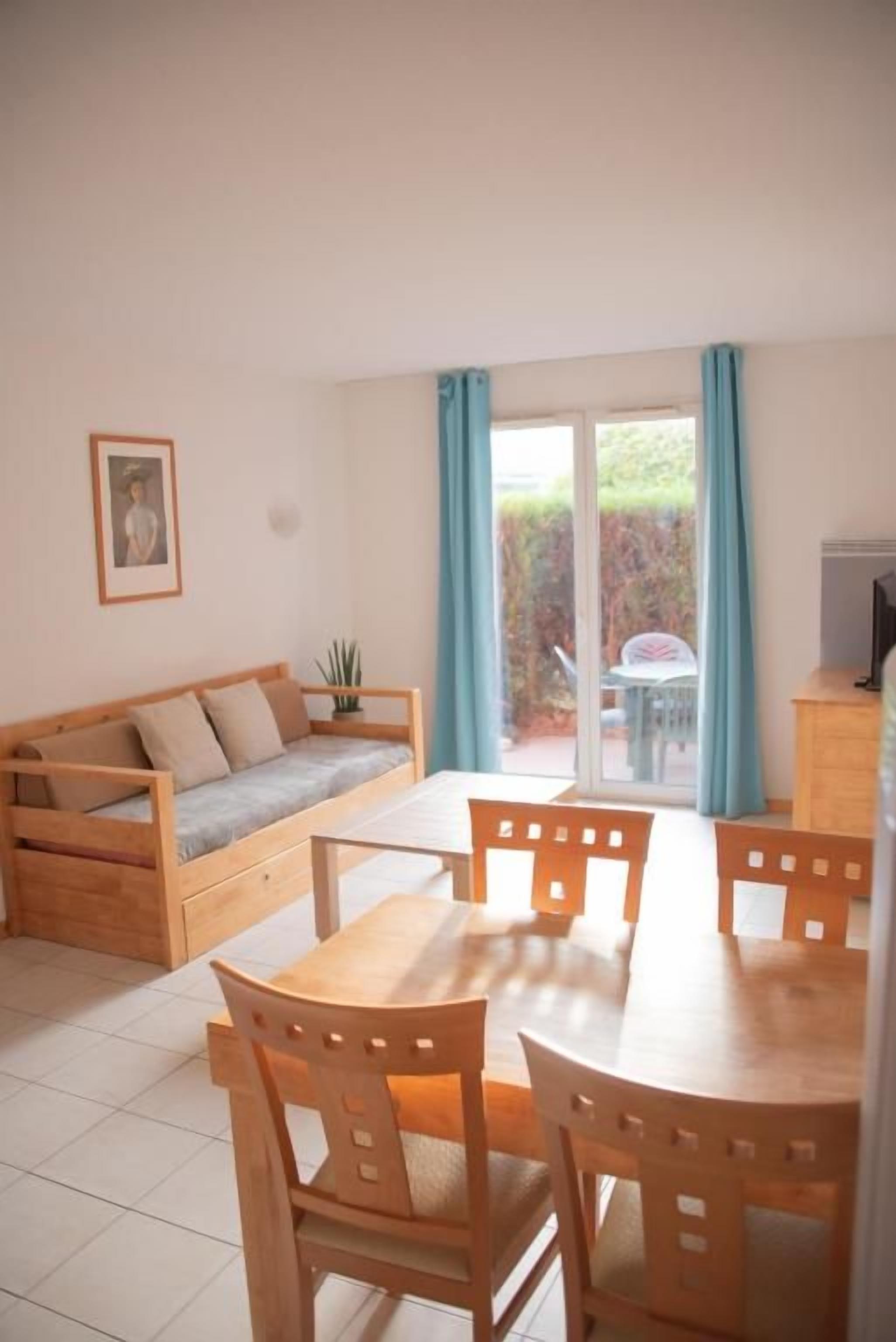 Een kamer met een houten eettafel en stoelen, een bank en een schuifdeur naar een terras.