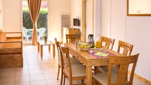 A dining area with a wooden table and chairs, a television on a stand, and a view of greenery through a glass door. - Residence le Royal Golf & Horse (Mooslargue)
