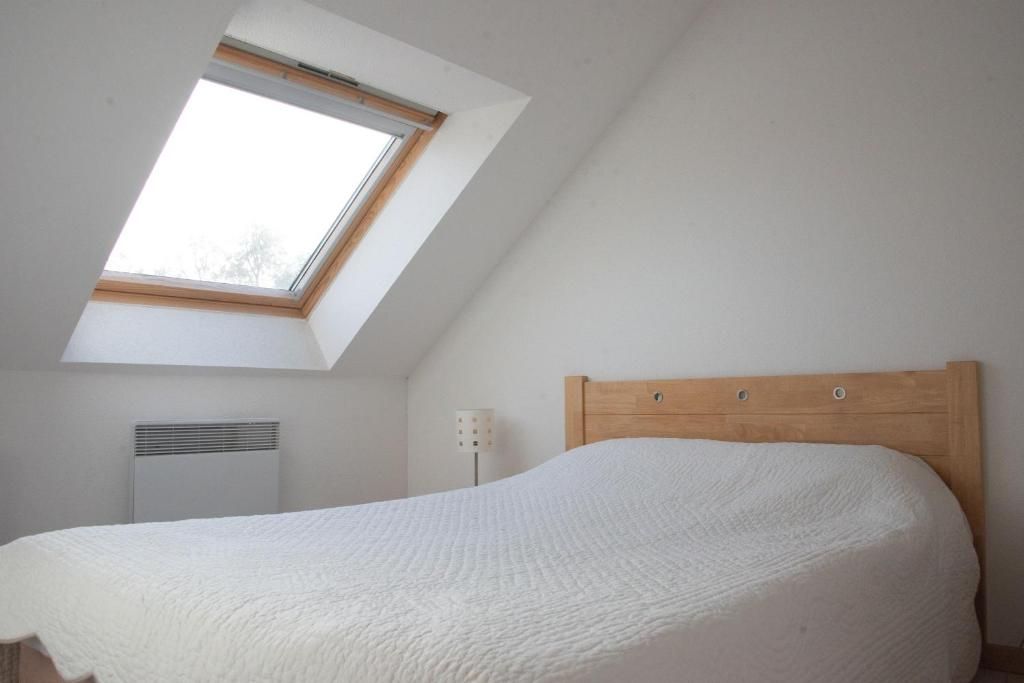 Une chambre avec un plafond en pente, un puits de lumière, un lit avec une tête de lit en bois et un radiateur fixé au mur.