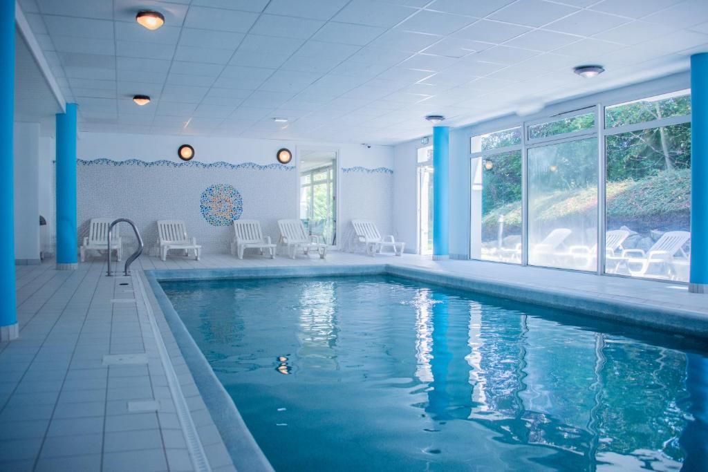 Una piscina interior con agua azul cristalina, rodeada de sillas reclinables blancas y suelo de baldosas.