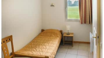 A small, single-bed room with a wooden bed, a bedside table with a lamp, a window with curtains, and a radiator.