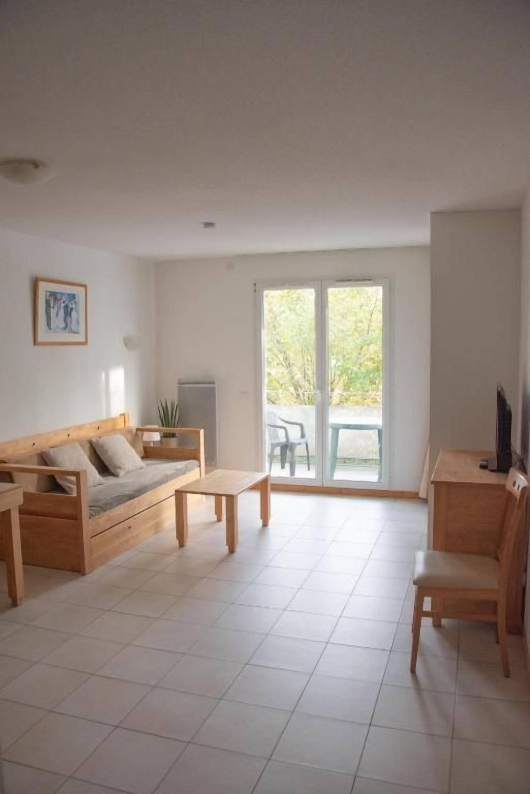 Una sala de estar con un sofá, una mesa de centro y una silla. Hay una puerta corrediza de vidrio que da a un balcón.