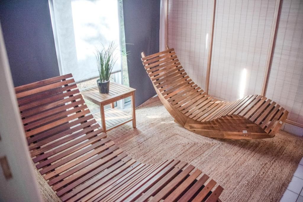 Une pièce avec une chaise à lattes en bois, une petite table sur laquelle est posée une plante en pot et une grande fenêtre.