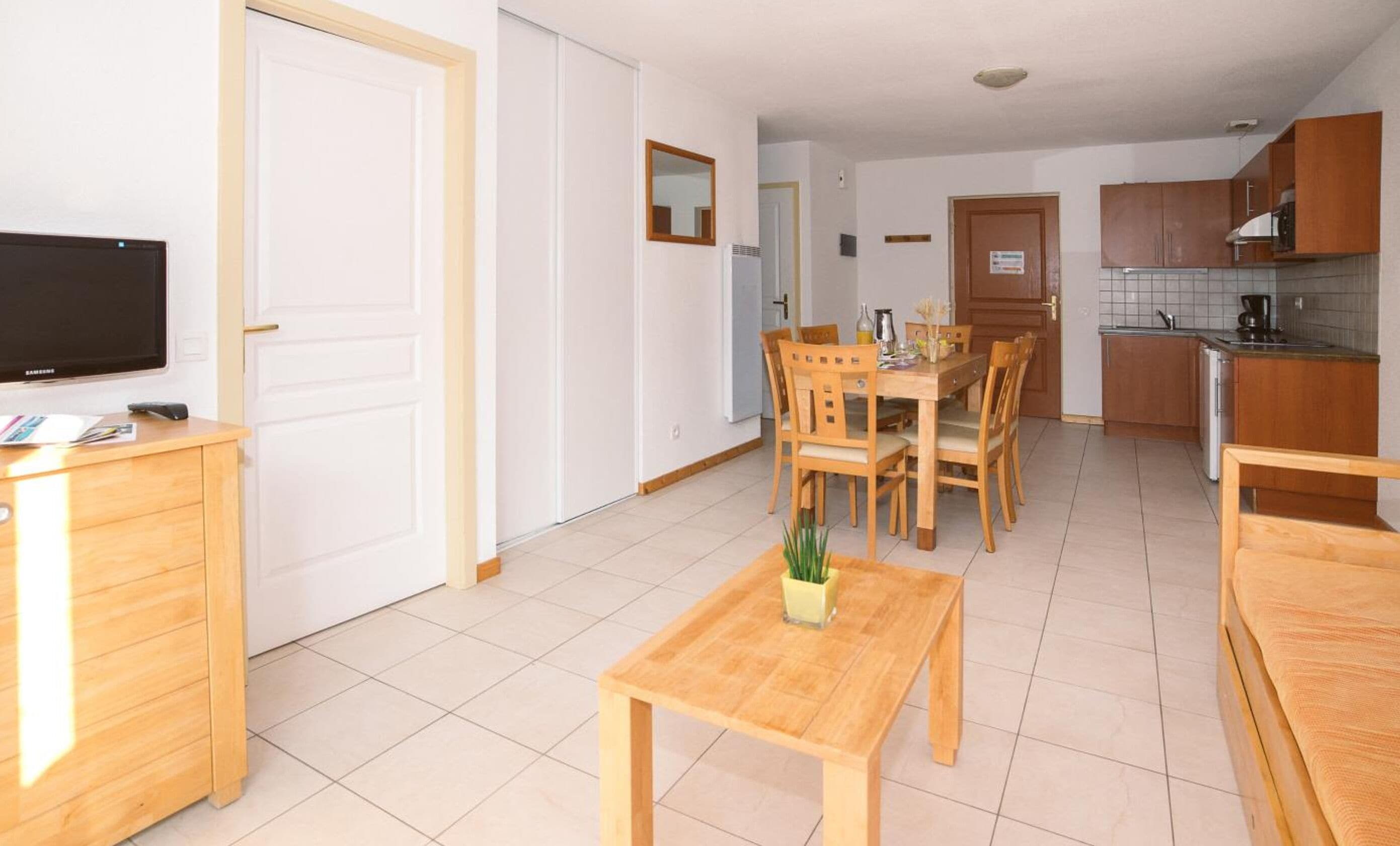 A modern apartment with a dining area, kitchen, and a TV on a wooden cabinet.