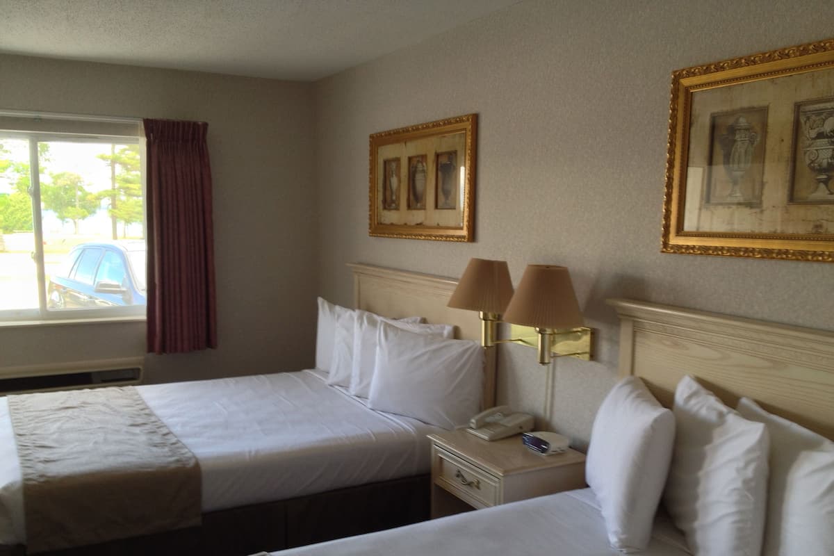 Une chambre d’hôtel avec deux lits, une fenêtre donnant sur l’extérieur, une table de chevet avec une lampe et des tableaux encadrés au mur.
