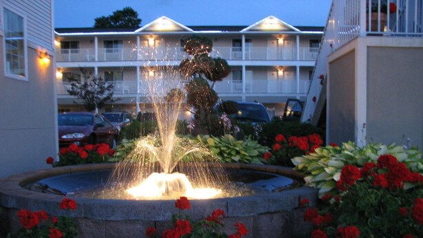 A fountain surrounded by potted red flowers, with a building in the background. - Parkside Inn Bridgeview (Mackinaw City)