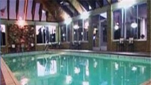 An indoor swimming pool with tiled edges, a tiled floor, and a ceiling with visible beams. - Parkside Inn Bridgeview (Mackinaw City)