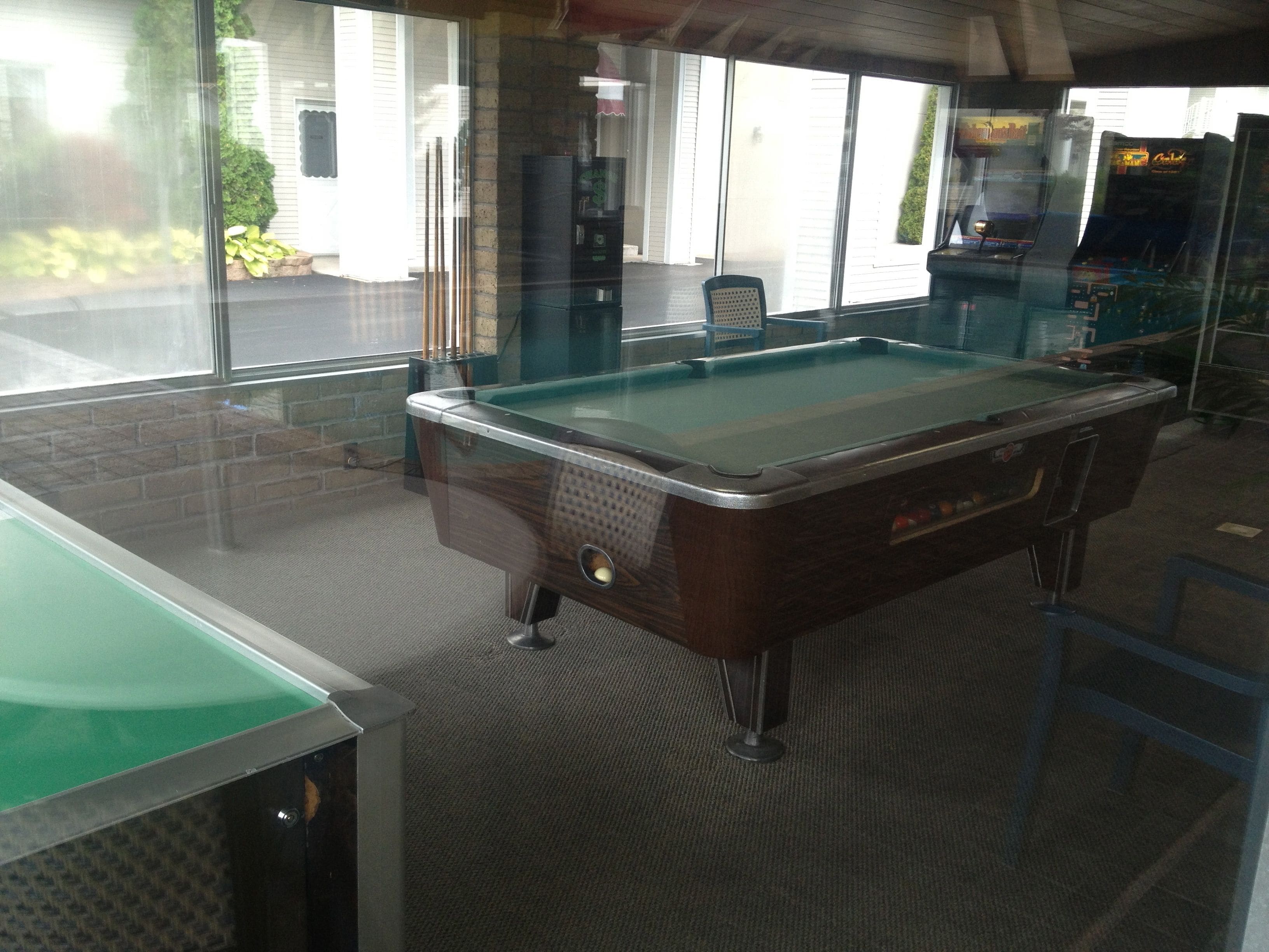 A pool table in a room with a carpeted floor and a window.