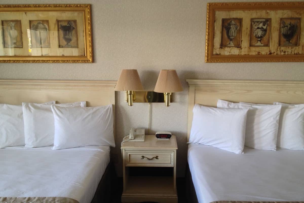 Une chambre d’hôtel avec deux lits, une table de chevet avec une lampe, un téléphone et des œuvres d’art encadrées accrochées au mur.