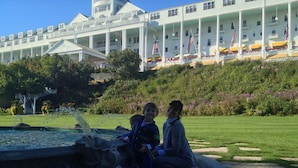 A large building with multiple balconies and flags, a fountain, and a well-maintained lawn. - Parkside Inn Bridgeview (Mackinaw City)