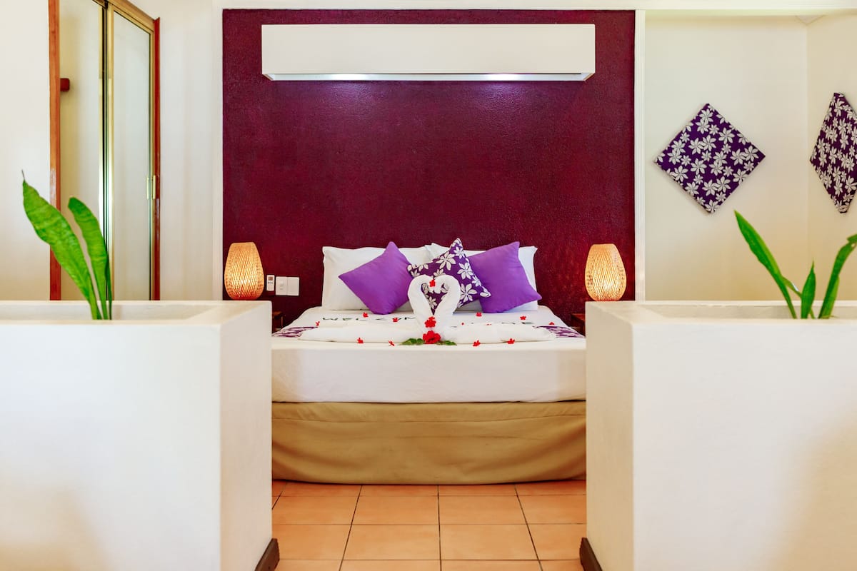 A neatly arranged hotel room with a bed centered between two white nightstands, each with a lamp. The room features a dark red headboard and two decorative wall hangings.
