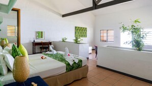 Een hotelkamer met een bed, een bureau, een stoel, een klein tafeltje, een plant en een raam met jaloezieën.